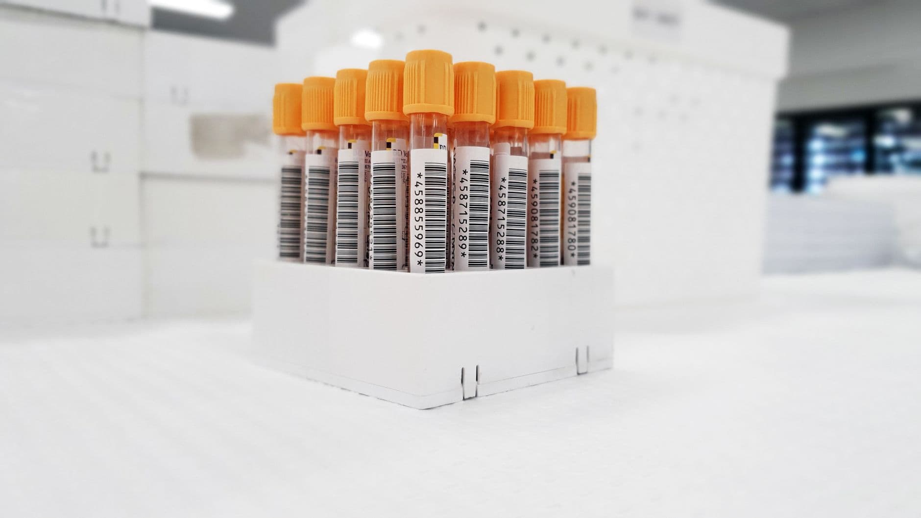 Provrör med streckkoder och orangea lock i ett stativ på ett laboratorium